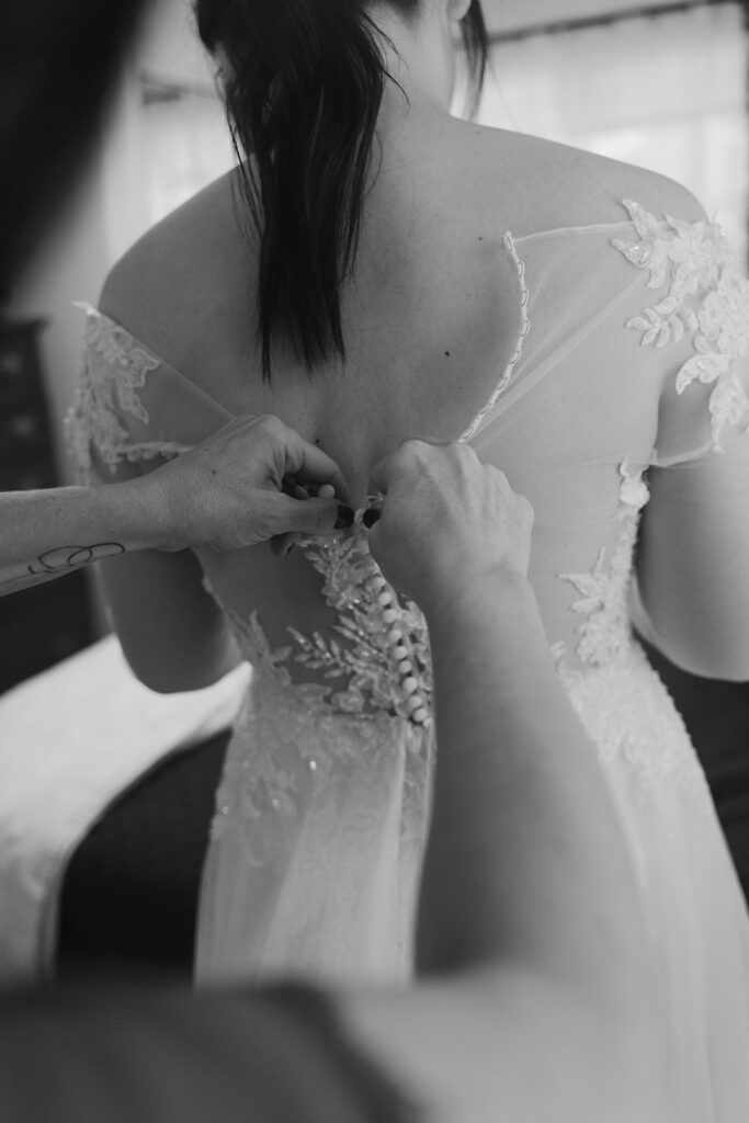 Black and white Photo of bride having her dress buttoned from the back