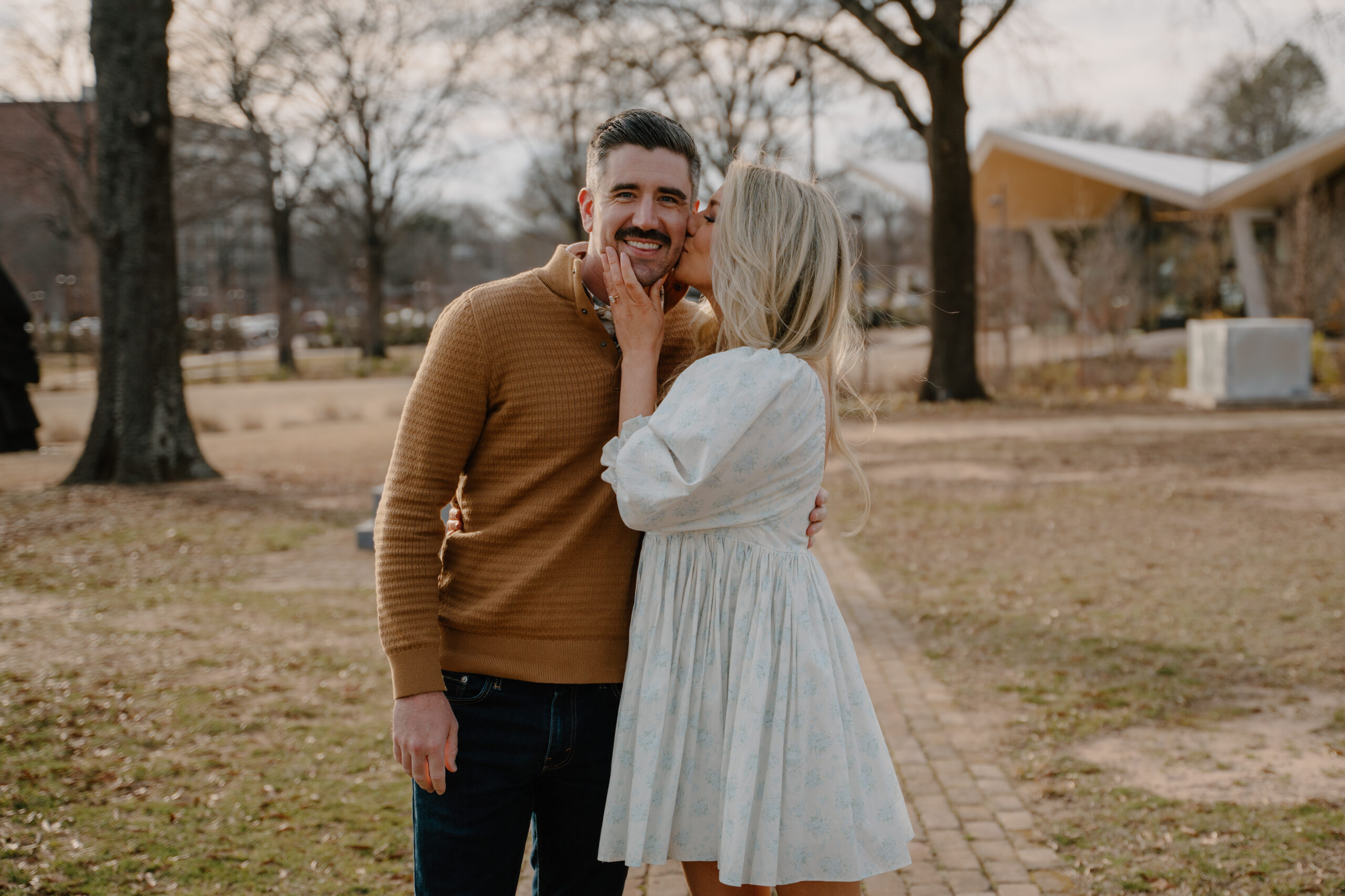 photo of girlfriend kissing boyfriend on the cheek and showing off her engagement ring