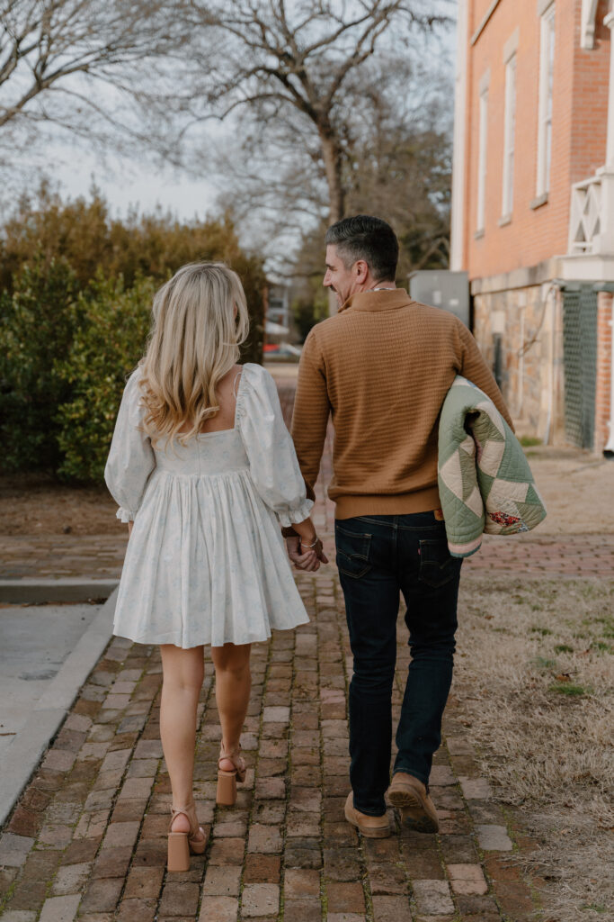 photo of engaged couple walking with a quilt behind the Military History Museum in Little Rock