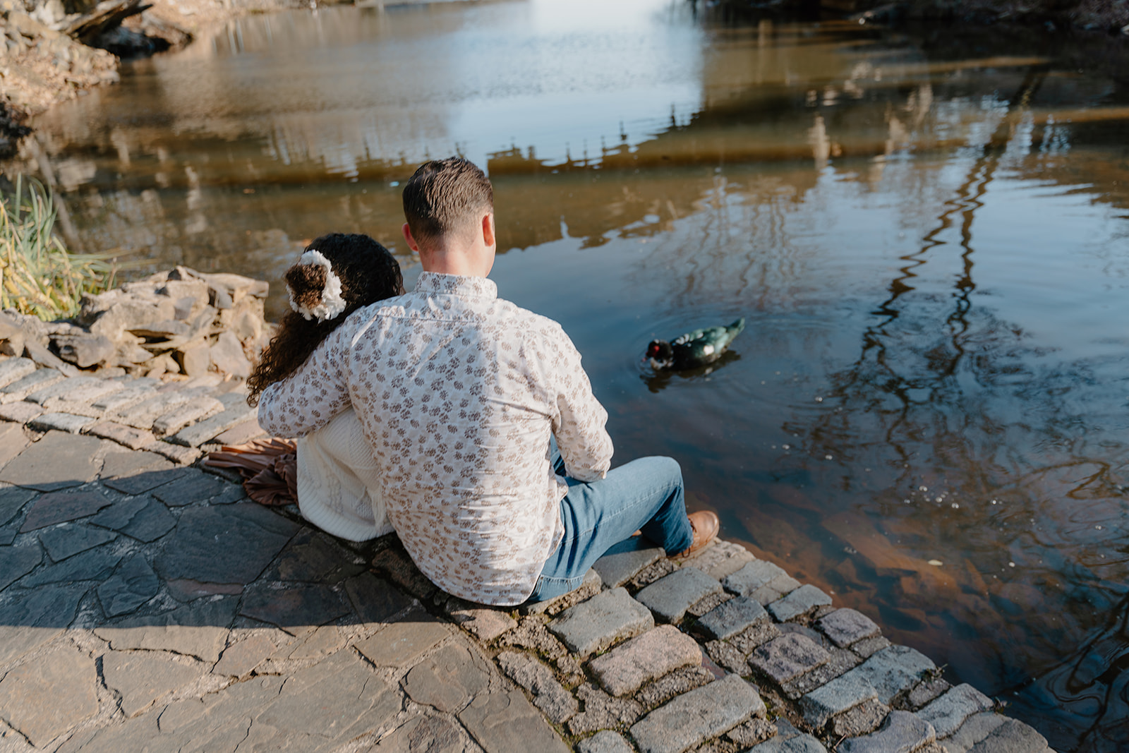 photo of couple snuggling sitting by the edge of the water