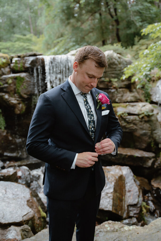 photo of groom buttoning his coat before the first look