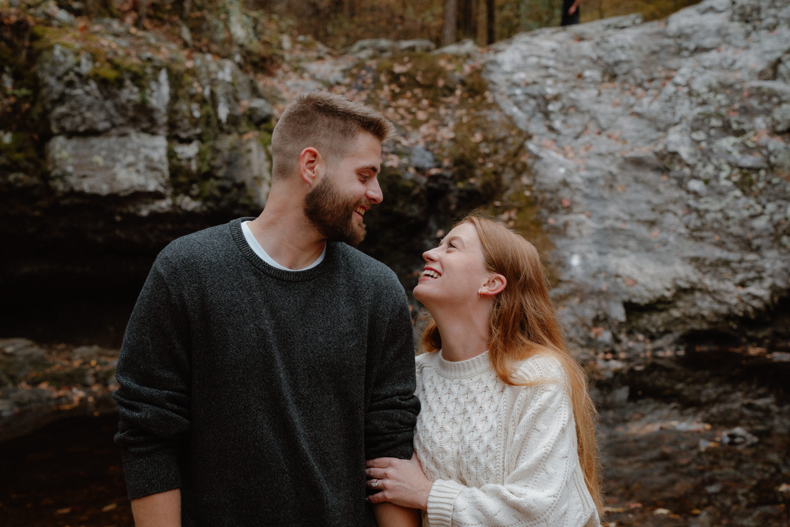 Couple linking arms and smiling at each other in front of a boulder