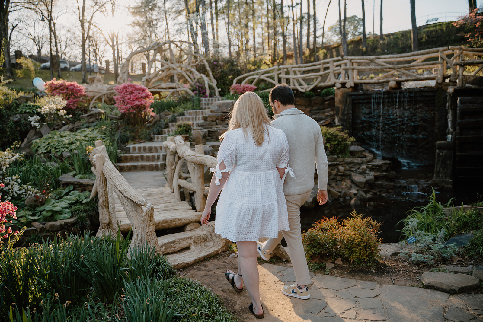 photo of engaged couple walking next to a waterfall and flowers and a bridge