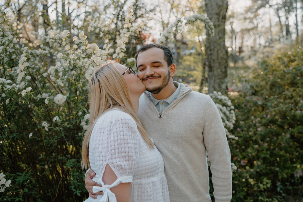 photo of girl kissing fiance on the cheek next to flowers