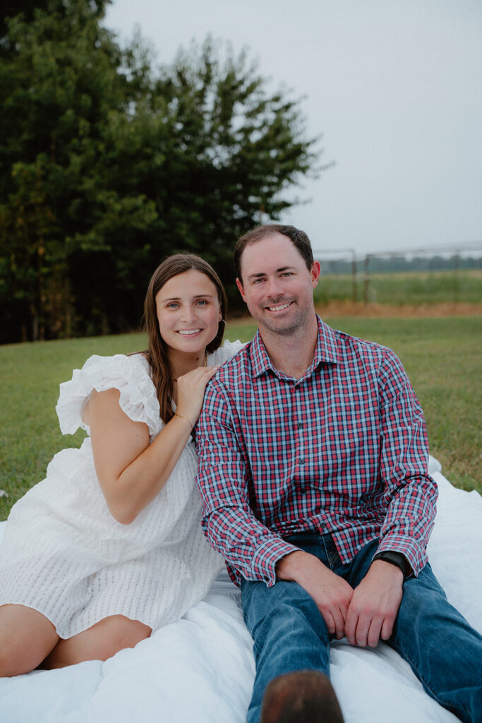 photo of engaged couple sitting on a picnic blanket